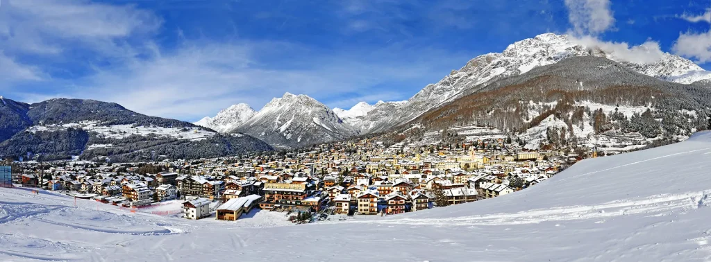 Panorama invernale di un villaggio di montagna innevato circondato da cime alpine.