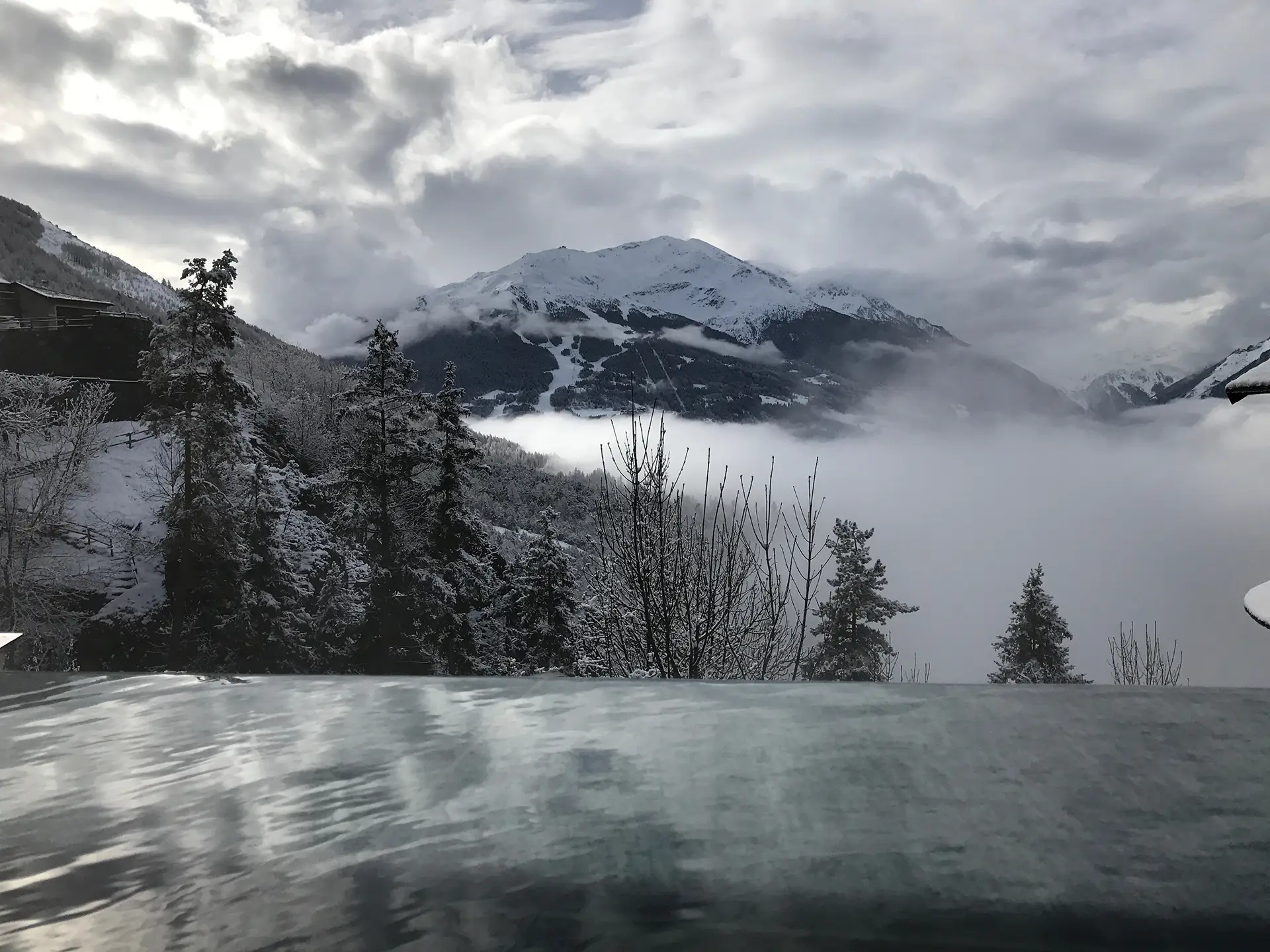 Vista panoramica di montagne innevate e alberi con nebbia che copre la valle.