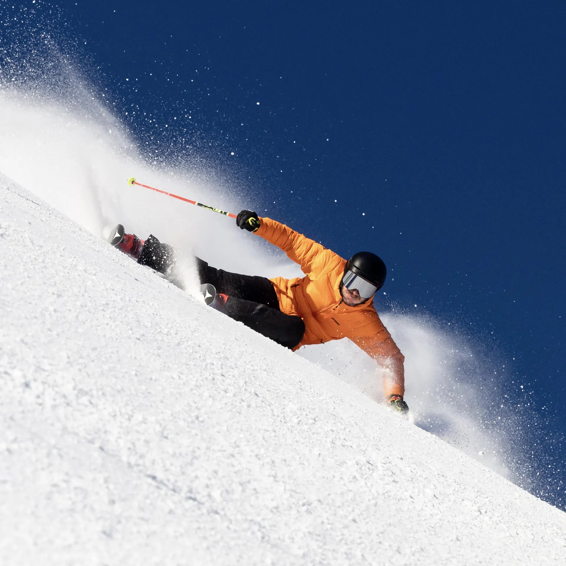 Scialpinista in giacca arancione scende velocemente una pista innevata.