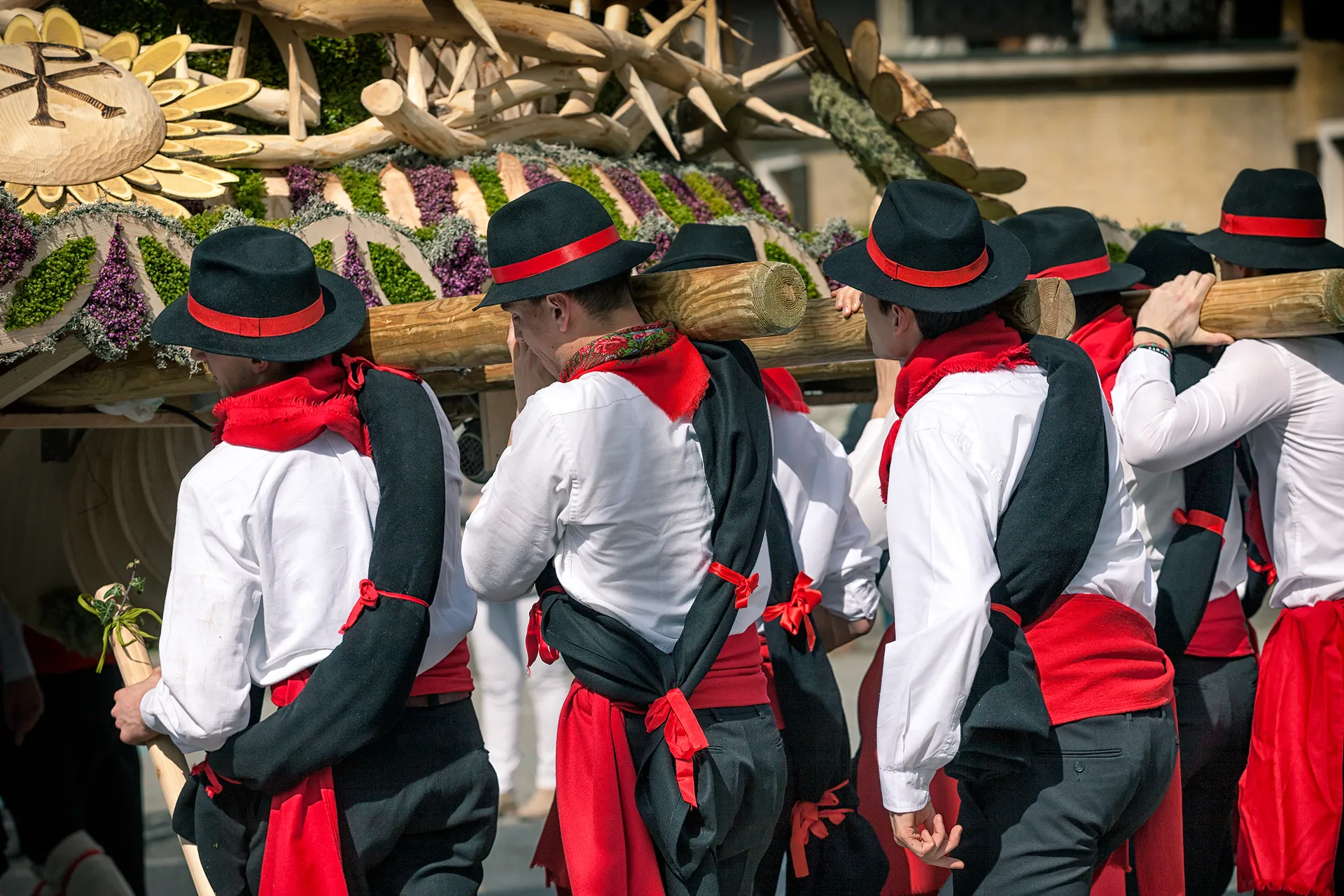 Persone in abiti tradizionali trasportano una struttura decorativa in legno.