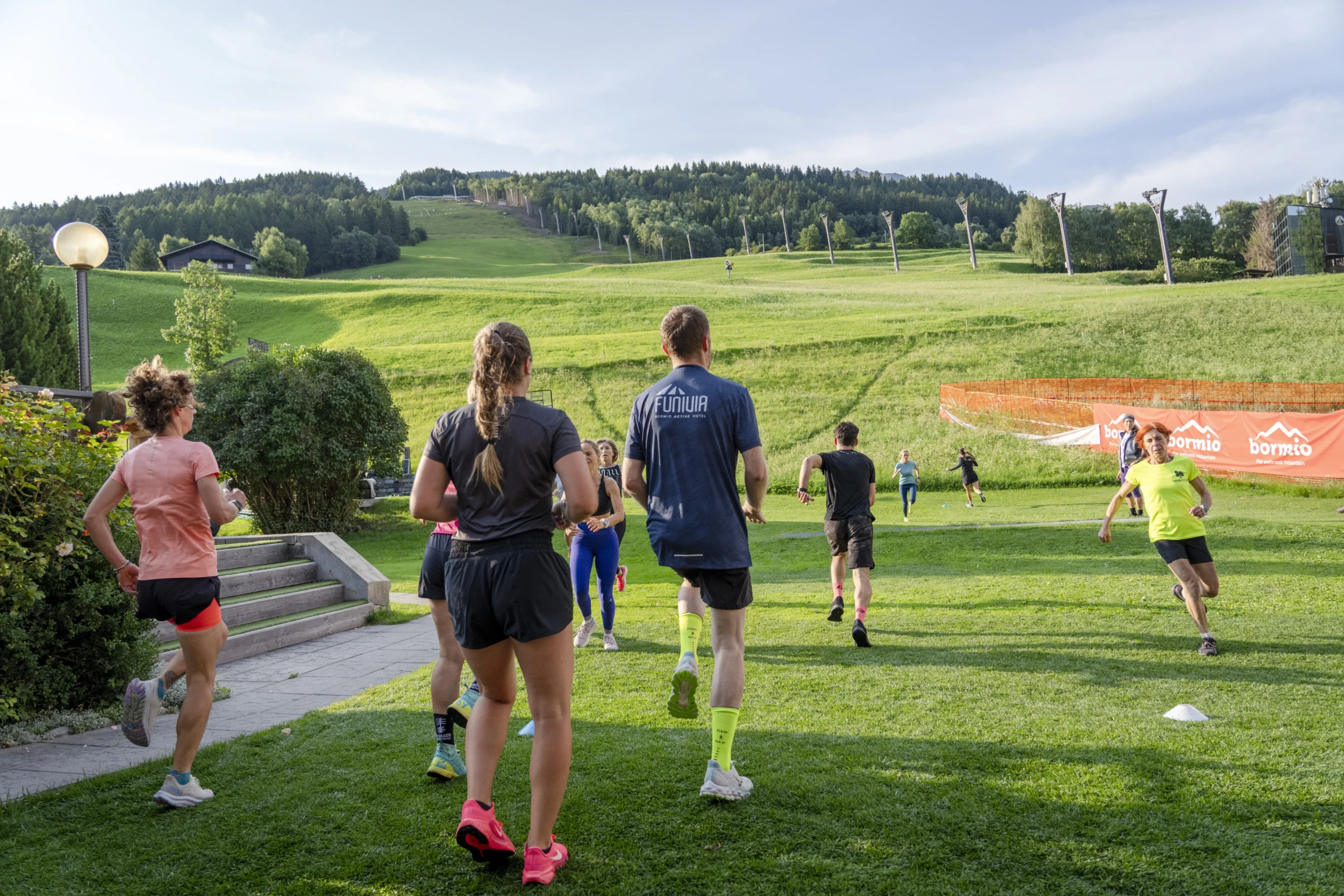 A group of people jogging on a grassy field with hills and trees in the background.