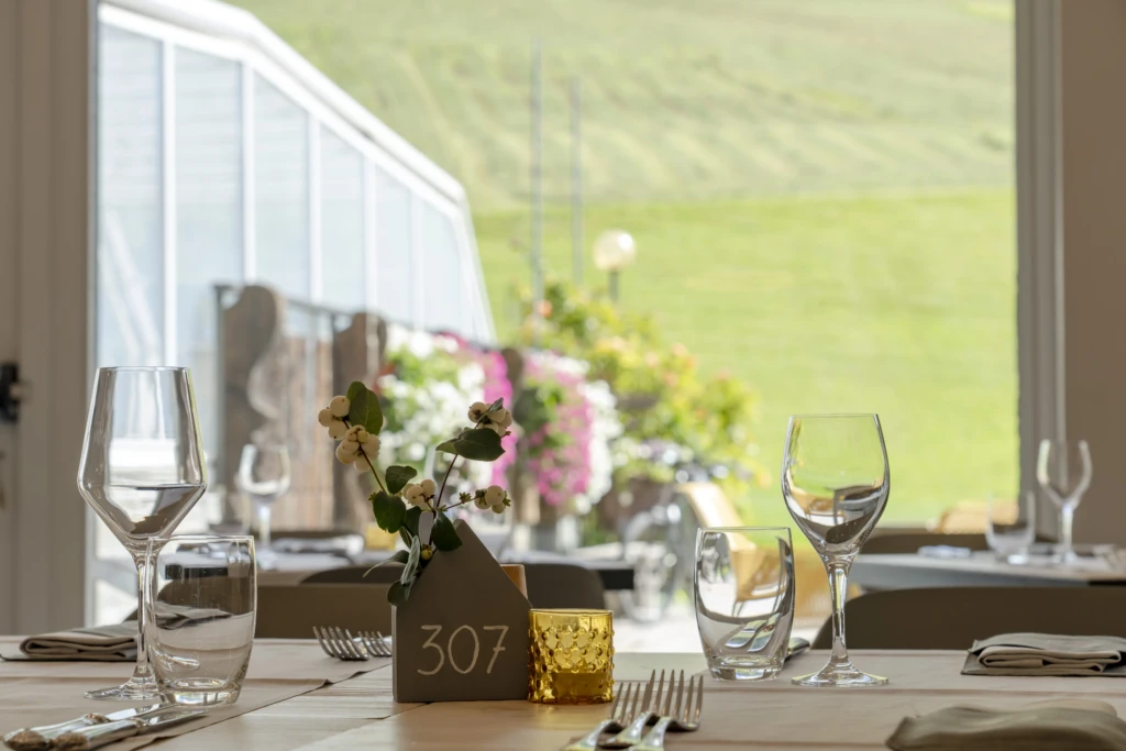 Tavola apparecchiata con vista su giardino fiorito e colline verdi.