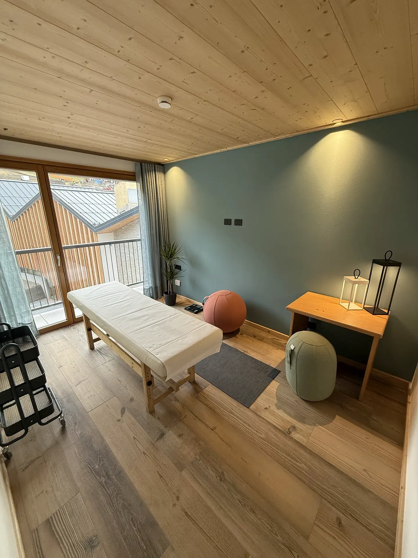 A cozy massage room with a wooden table, yoga balls, and a large window.