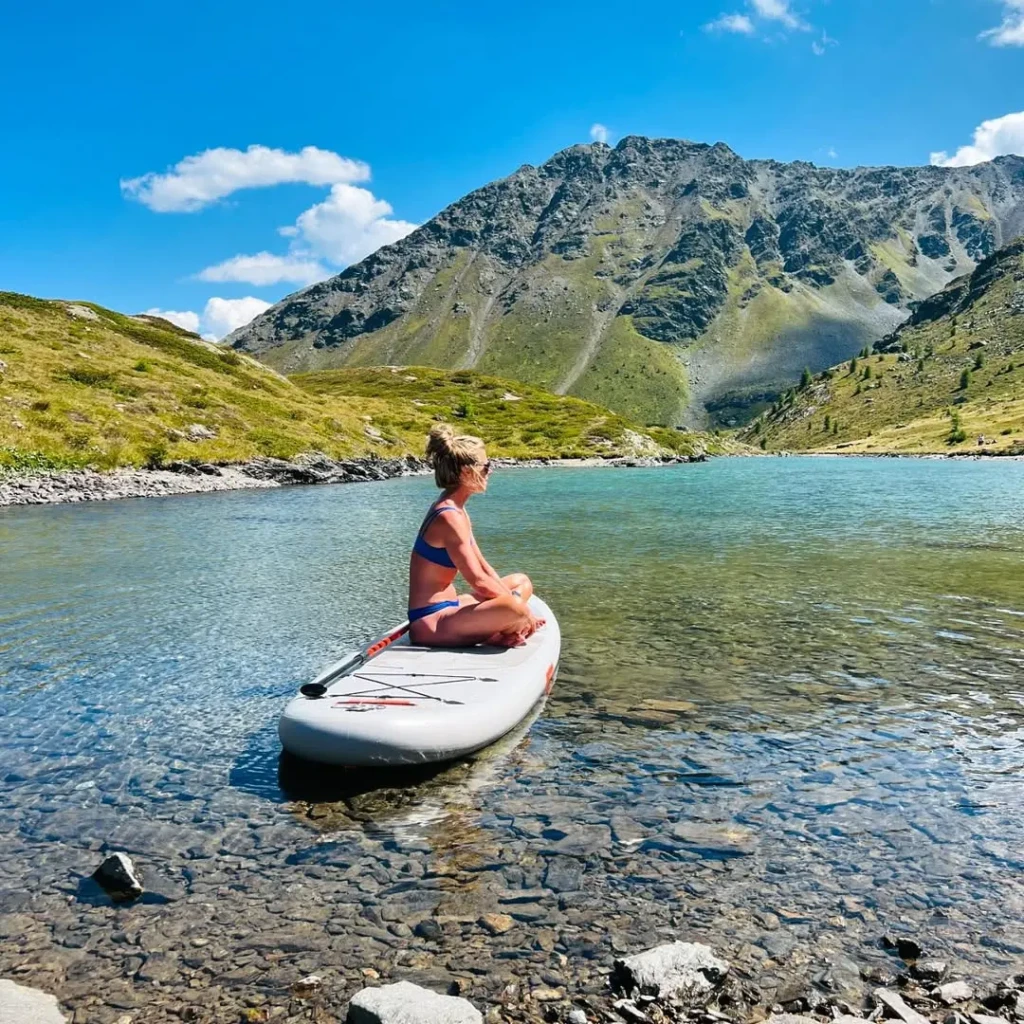 A person sits on a paddleboard on a clear lake with a mountain backdrop.