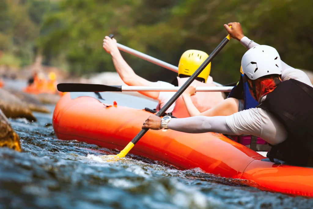 People wearing helmets and life jackets paddling in an orange raft on a river.