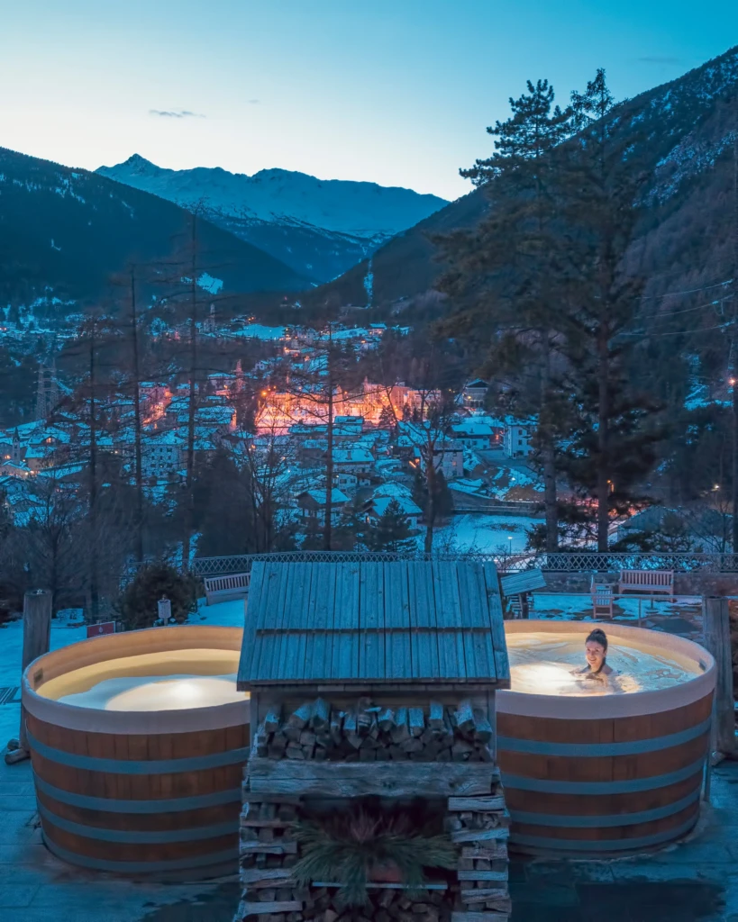 Panorama invernale di montagna con una persona che si rilassa in una vasca idromassaggio.