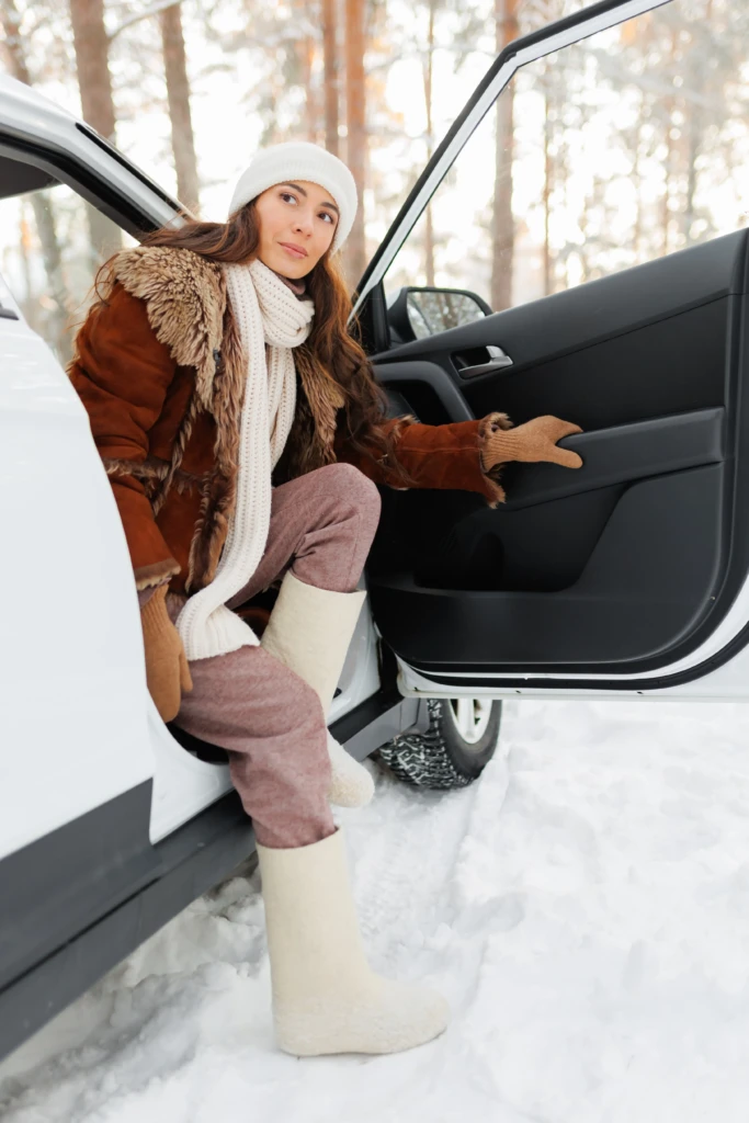 Donna con abbigliamento invernale scende dall'auto in un paesaggio innevato.