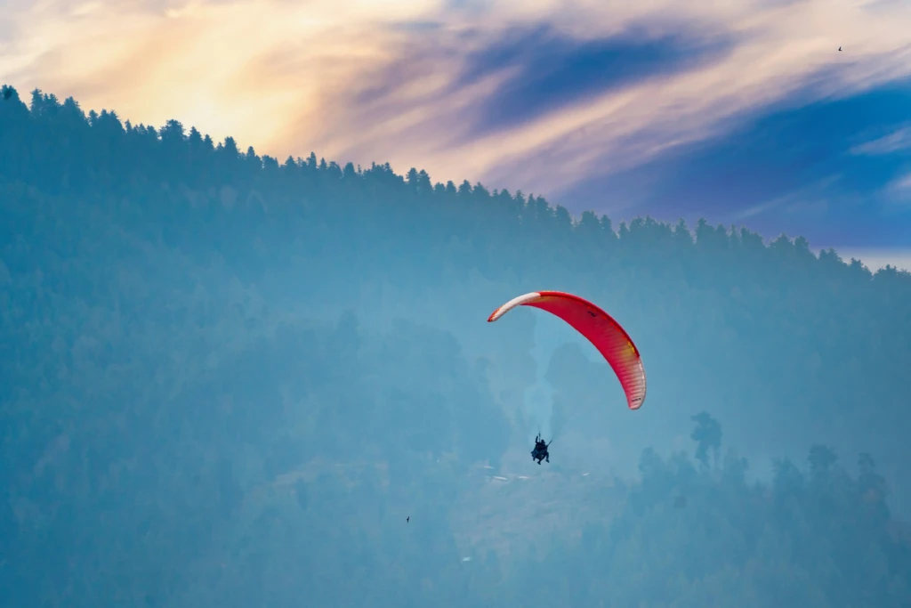 A paraglider soaring above forested hills at sunset.