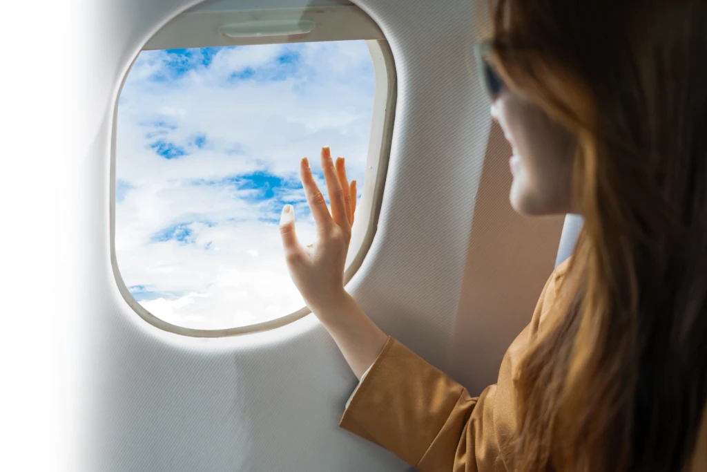 Persona sorridente guarda fuori dal finestrino dell'aereo verso le nuvole.