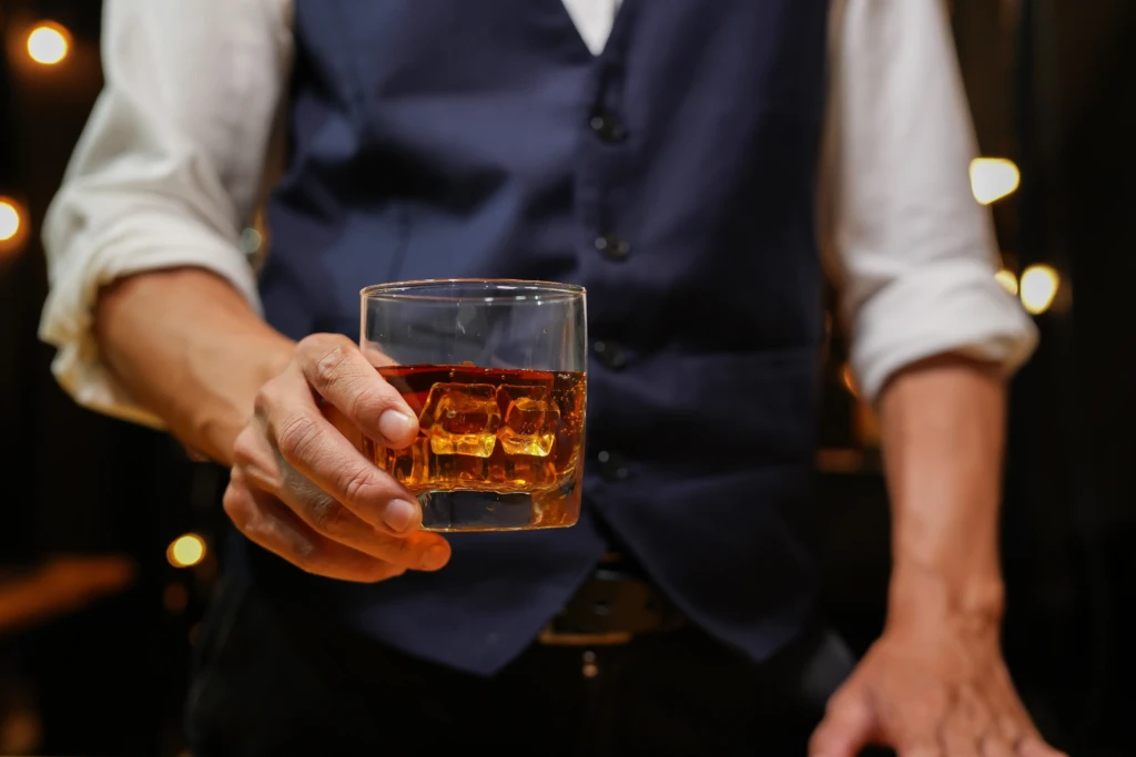 A person holding a glass of whiskey with ice cubes.