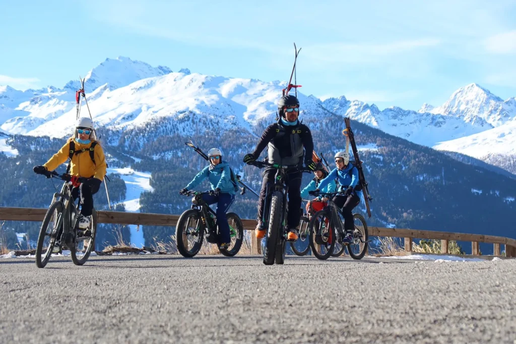 Ciclisti su mountain bike con sci su uno sfondo di montagne innevate.