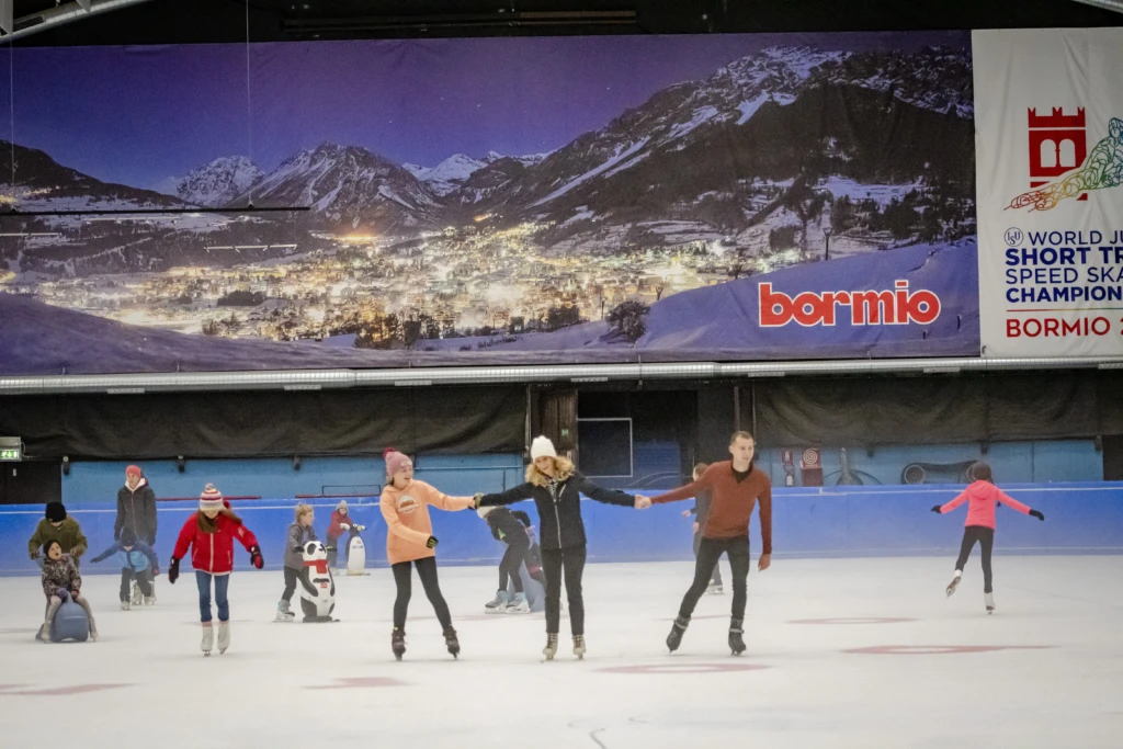 Pattinatori su una pista di ghiaccio coperta con un grande murale di montagna sullo sfondo.
