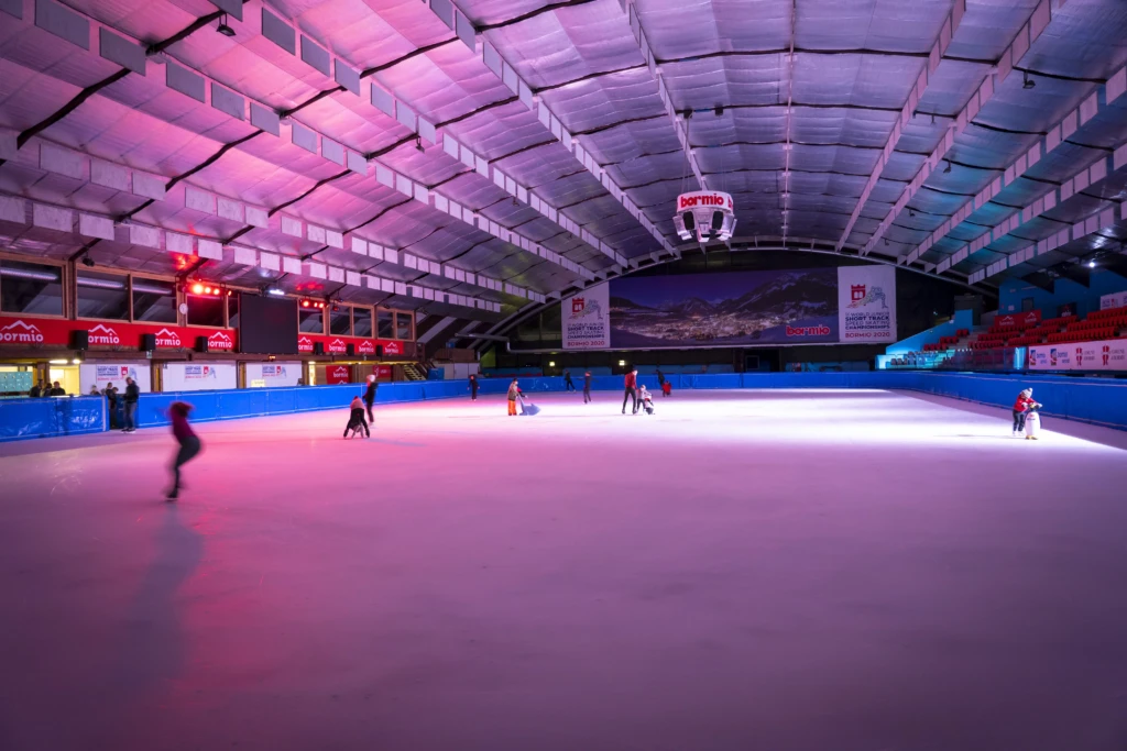 Pattinatori su una pista di pattinaggio coperta con luci colorate.