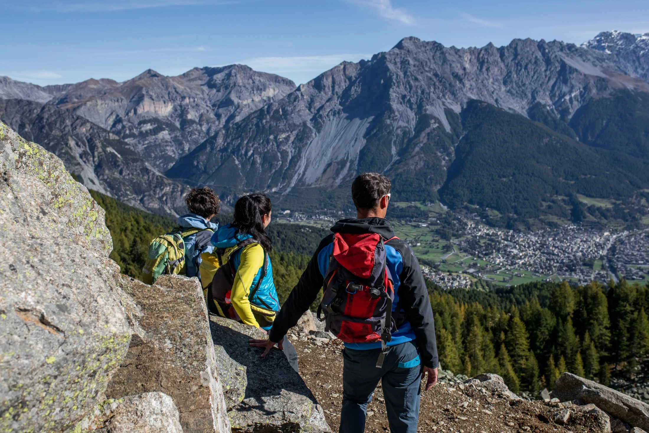 Three hikers with backpacks enjoy a mountain view.