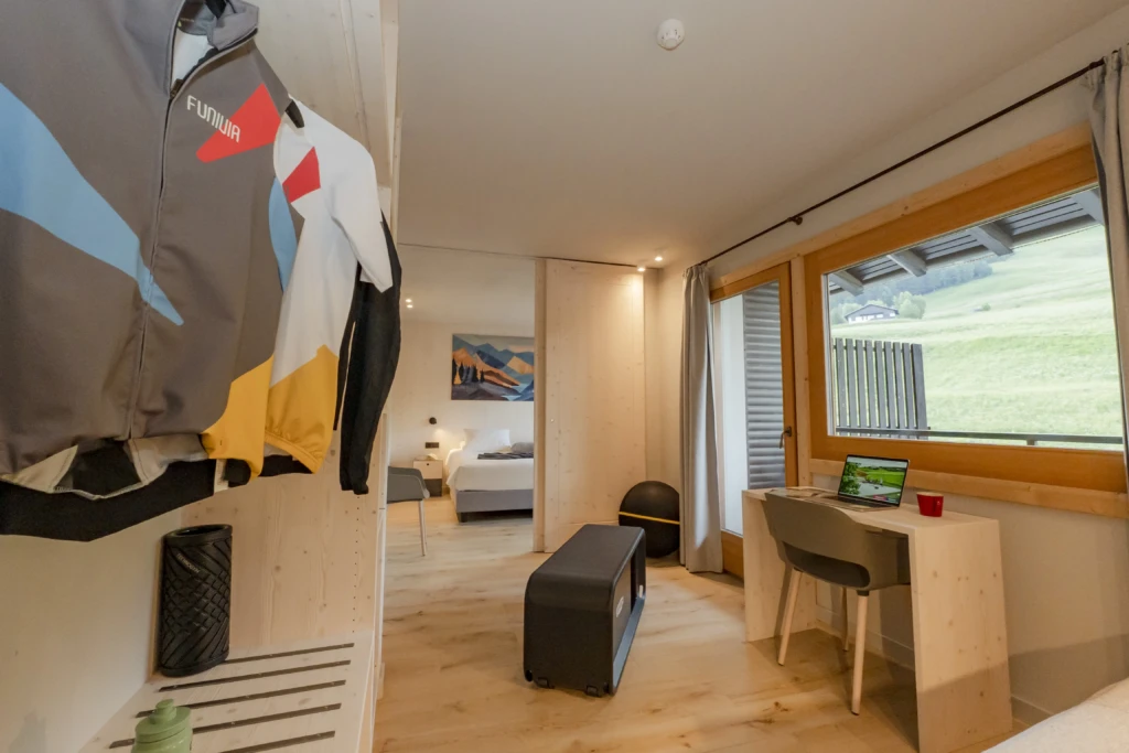 Camera accogliente con vista sulle colline, scrivania con laptop e giacche appese.
