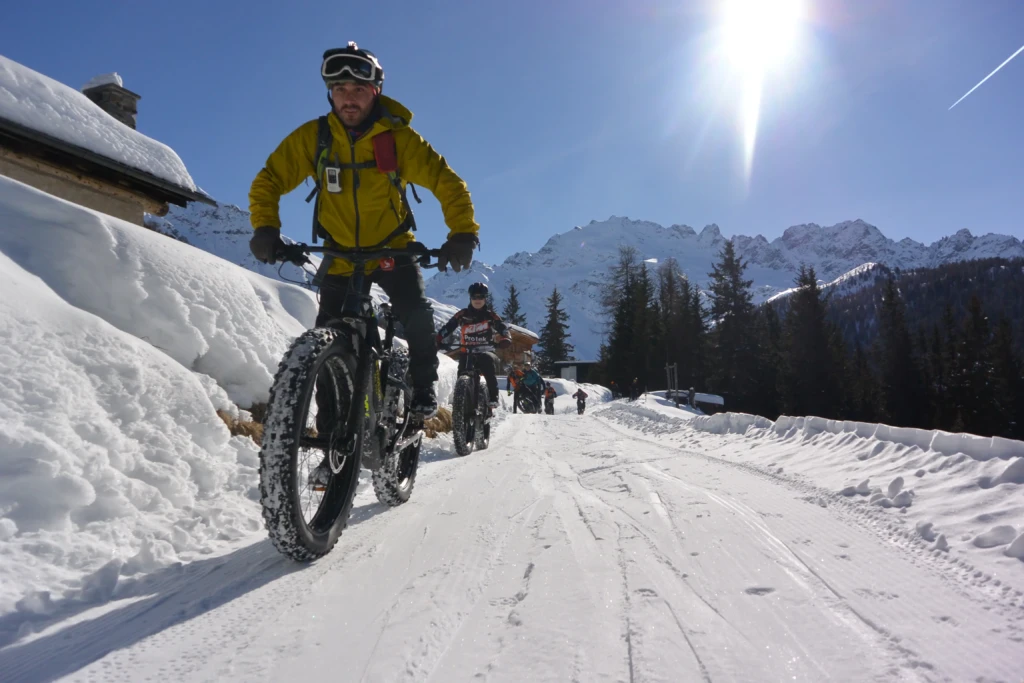 Ciclisti su fat bike percorrono un sentiero innevato in montagna sotto il sole splendente.
