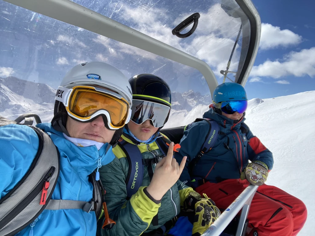 Tre sciatori su una seggiovia in montagna con indumenti invernali colorati.