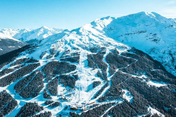 Panorama aereo di una montagna innevata con piste da sci e foreste.