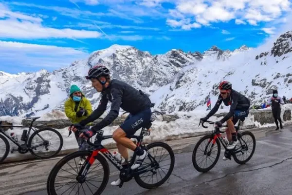 Cyclists riding along a snowy mountain road with a scenic backdrop.