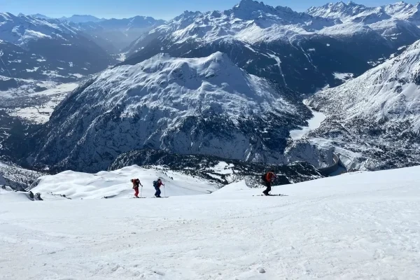 Sciatori che scendono una montagna innevata con un panorama montuoso sullo sfondo.