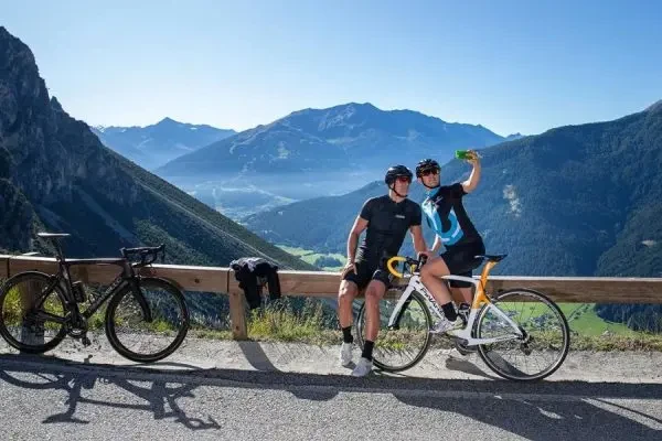 Two cyclists take a selfie with a scenic mountain view in the background.