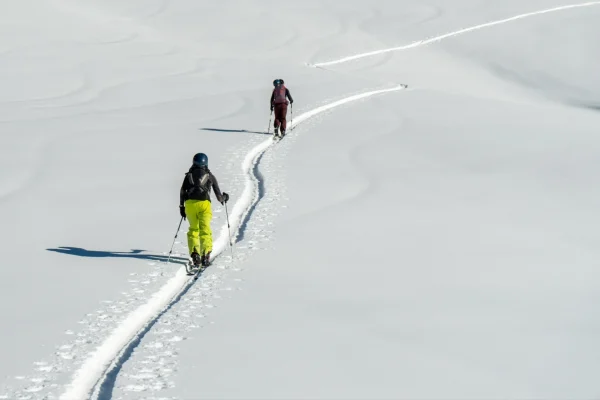 Two people skiing uphill in a snowy landscape.